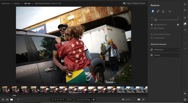 Adult holding child wearing red star-patterned jacket near parked vehicles and storefront.