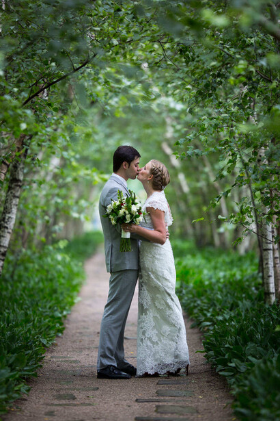 Bride and groom kissing under a green leafy tunnel archway on a brick pathway.