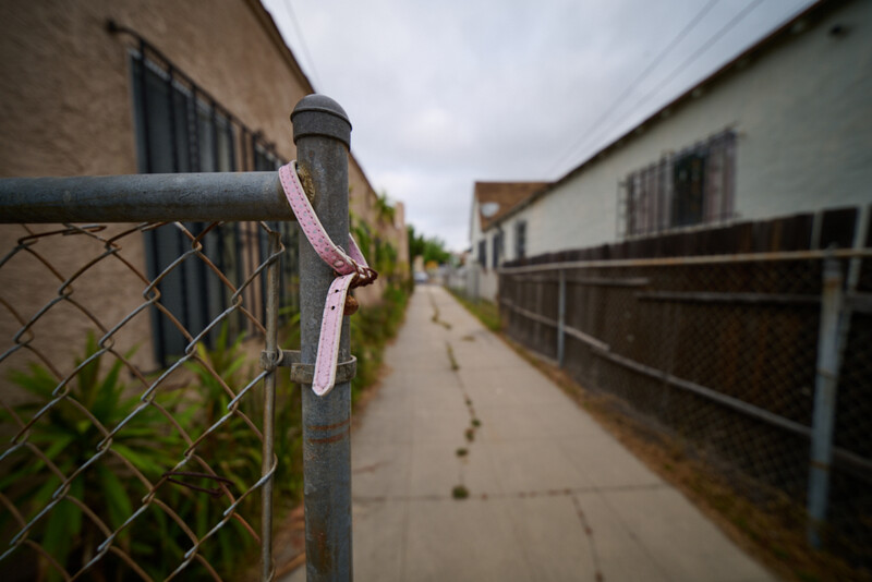 Pink ribbon tied to a chain-link fence post along an empty residential alley.