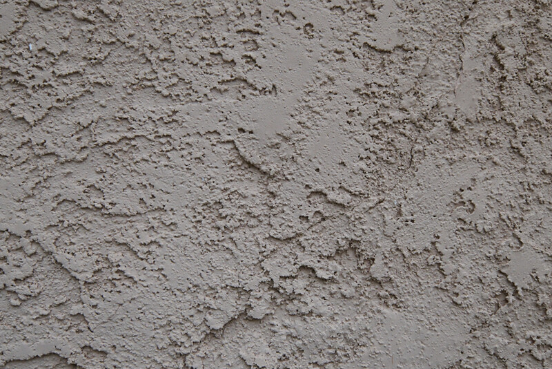 Close-up texture of rough concrete or cement surface with uneven pitting and weathering patterns.