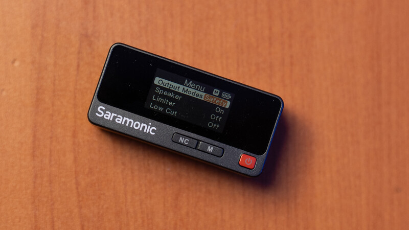 Saramonic wireless microphone receiver displayed on an orange wooden surface showing menu interface on screen.