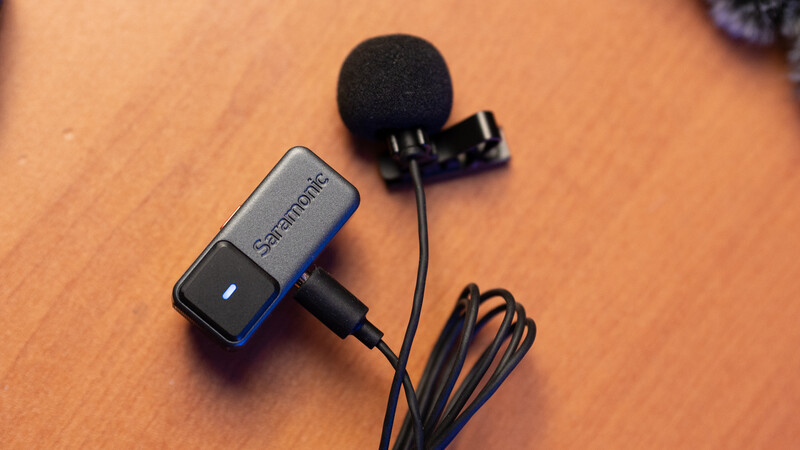 Saramonic lavalier microphone with windscreen and cable on wooden surface.