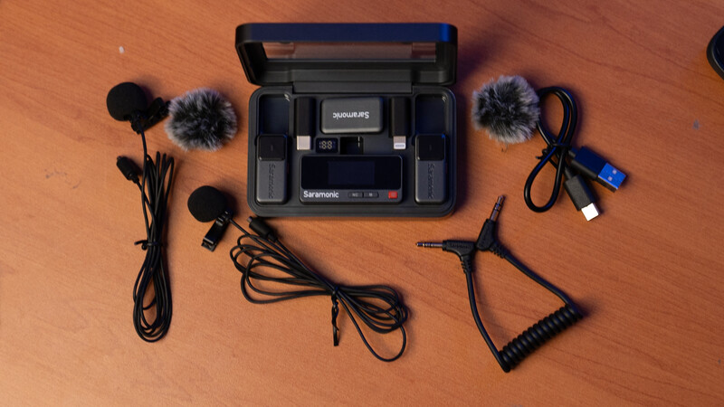 Flat lay of video production gear including a portable recorder with windscreen mics, XLR cables, and accessories on a wooden surface.