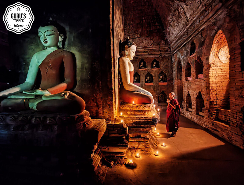 Buddhist statue illuminated in green light inside a temple with candlelit shrine niches.