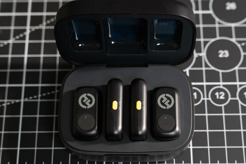 Wireless microphone system with two transmitters and receiver in open charging case against grid background.