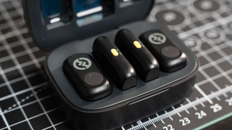 Four wireless earbuds with charging case on a grid ruler surface.