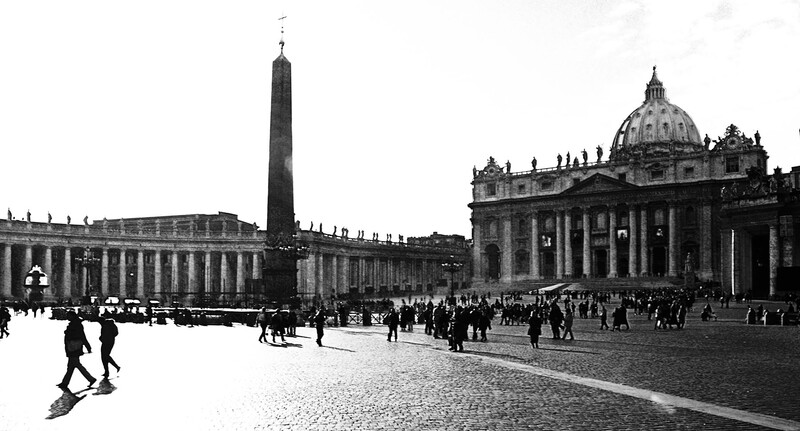 Historic black and white photograph of a grand plaza with classical architecture, obelisk, and basilica with dome.