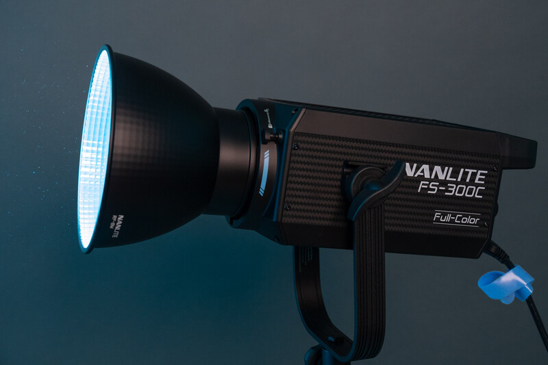 Vanlite F-300C Full-Color LED spotlight with illuminated fresnel lens and power cable against dark blue background.