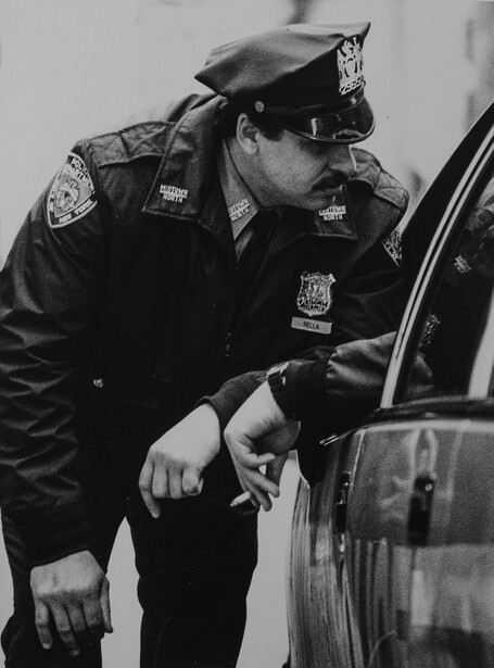 Police officer in uniform leaning toward a vehicle window in black and white.