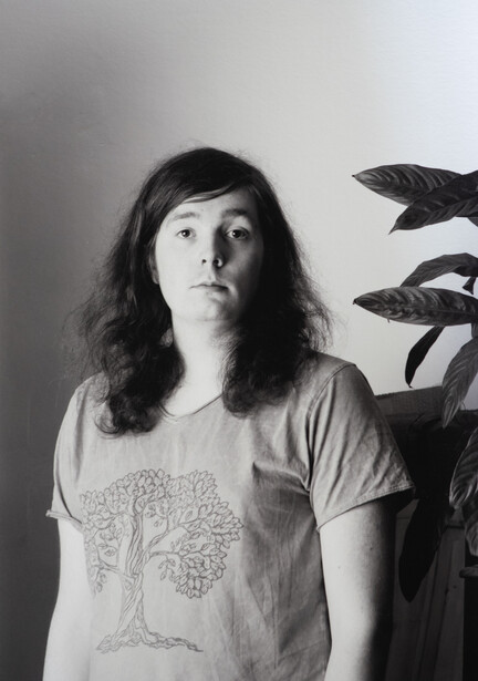 Black and white portrait of a woman with long dark hair wearing a graphic t-shirt, looking upward thoughtfully.