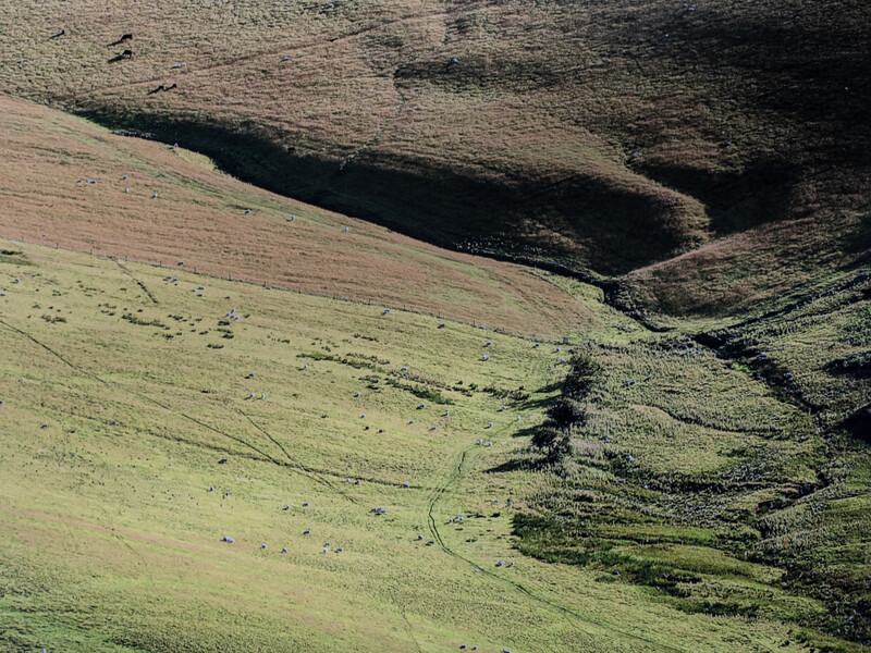 Aerial view of rolling hillsides with layered terrain in muted earth tones and green vegetation.