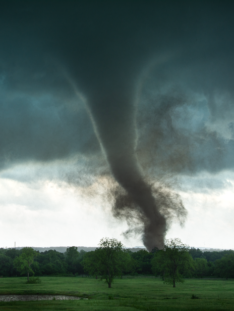 Tornado touching down across a green field under dark storm clouds.