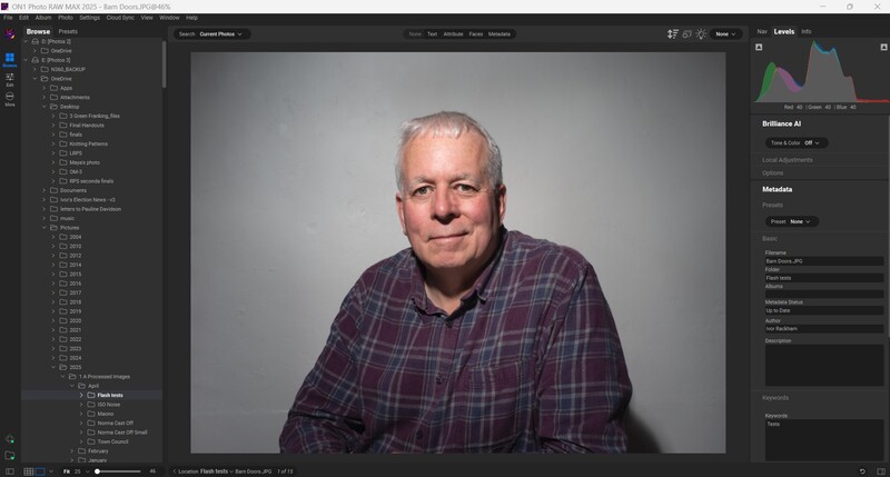 Headshot of an older man wearing a purple plaid shirt against a neutral gray backdrop.