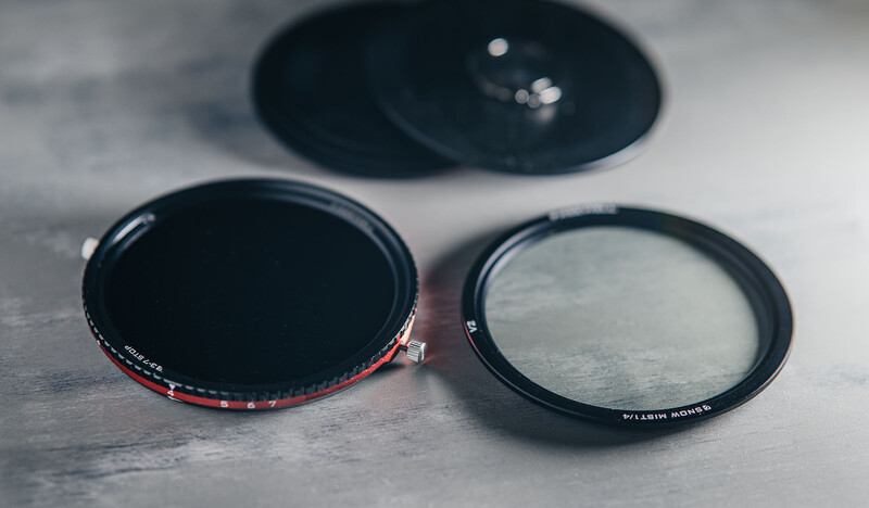 Three camera lens filters arranged on a textured gray surface, showing front and back views with lens caps.