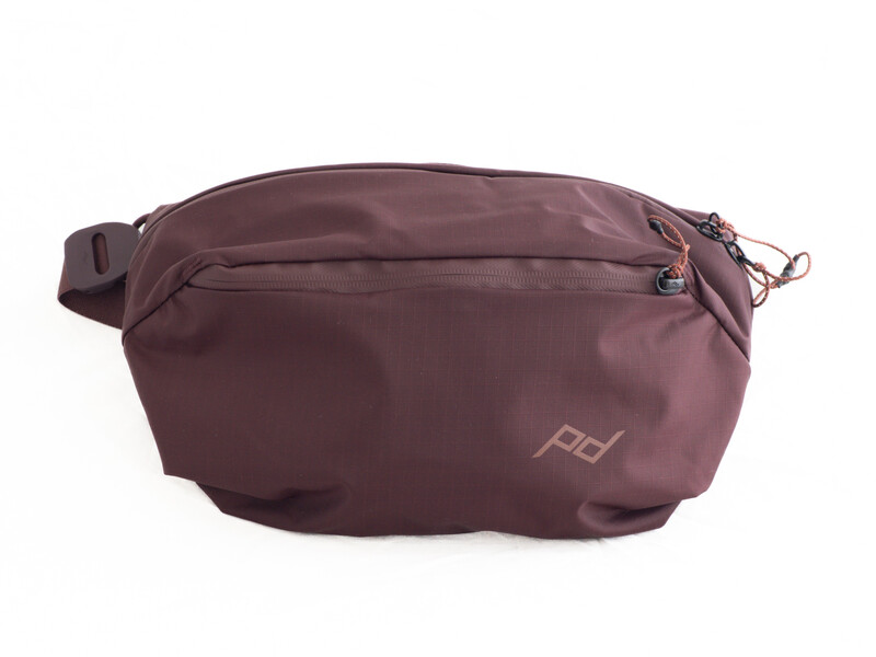 Burgundy waist pack with top zipper compartment and side attachment loops against white background.