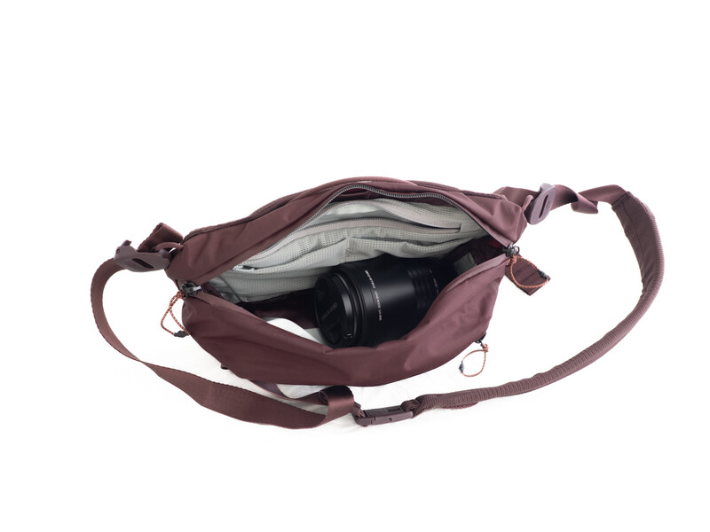 Burgundy canvas camera bag with shoulder strap open to reveal interior storage and black camera lens inside.