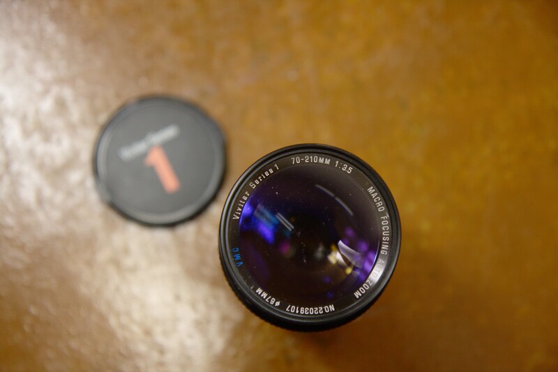 Vintage camera lens with purple-tinted glass and gray lens cap on warm-toned surface.