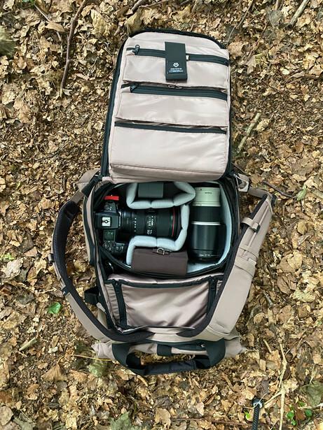 Overhead view of an open camera backpack with organized gear compartments on concrete ground.