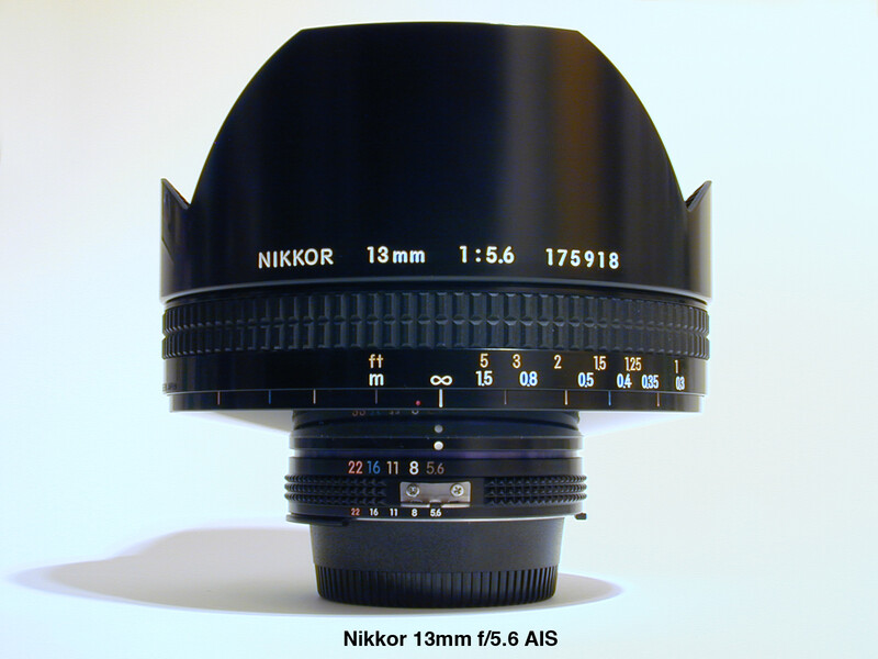 Nikkor 13mm f/5.6 AIS lens with hood mounted, displayed against white background.