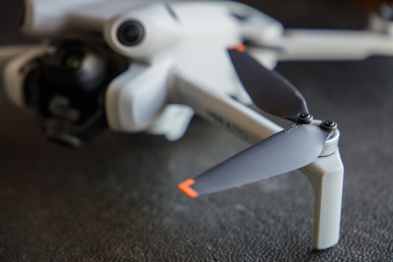Close-up of a white quadcopter drone with folded propeller arms and orange accents on a gray surface.