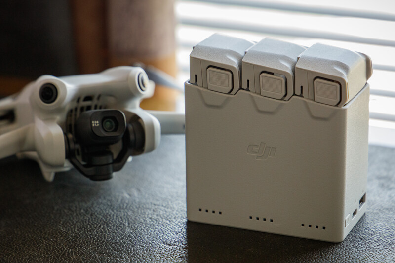 DJI drone with three intelligent flight batteries displayed beside it on a surface near a window.