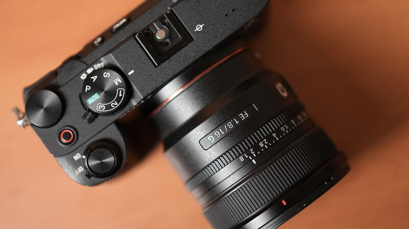 Top-down view of a mirrorless camera body with attached prime lens on warm tan background.