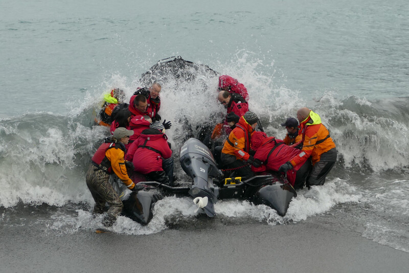 Rescue team in bright life jackets launching an inflatable boat through crashing waves.