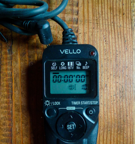 Vello digital timer and stopwatch device with LCD display showing zeroed time, mounted on wooden surface with blue cable.