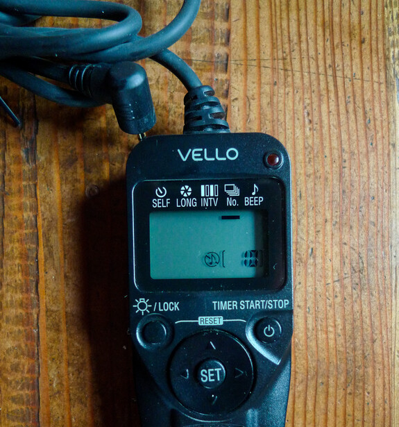 Vello camera light meter with blue cable on wooden surface.