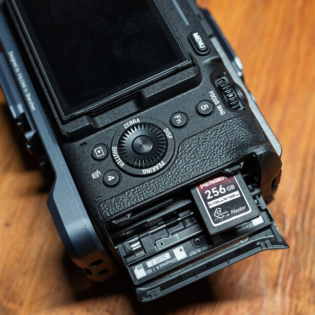 Professional camera body with articulating screen displayed on wooden surface, showing top-mounted controls and memory card slot.