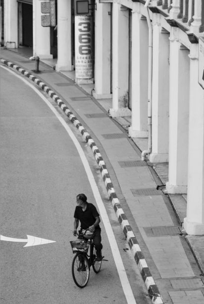 Cyclist riding on a curved street lined with white bollards and modernist building facades.