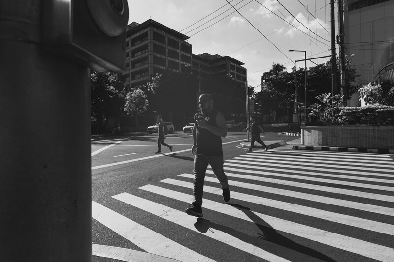 Businessperson crossing a zebra crossing in an urban intersection with strong shadows from buildings.