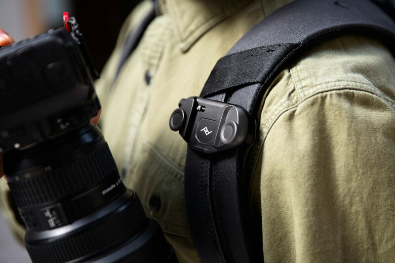 Camera strap attachment point mounted on khaki-colored camera bag with black camera lens visible on left side.