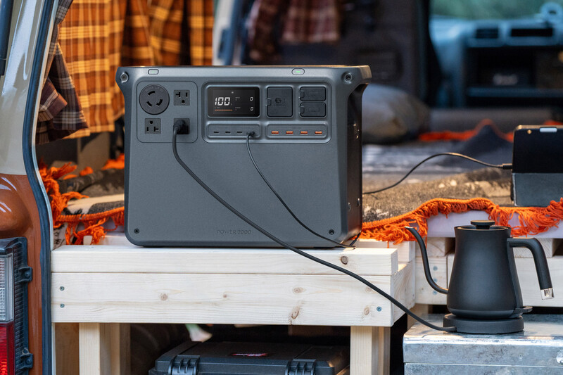 Portable power station with digital display sitting on wooden table in outdoor camping setup.