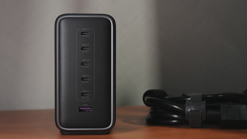 Black multi-port USB charging hub with six ports displayed vertically on wooden surface.
