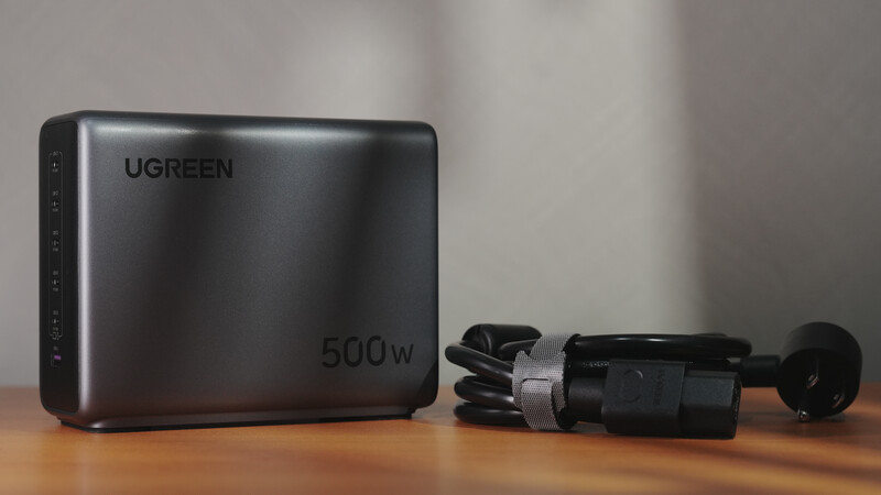 Ugreen 500W power supply with coiled black power cable on wooden surface.