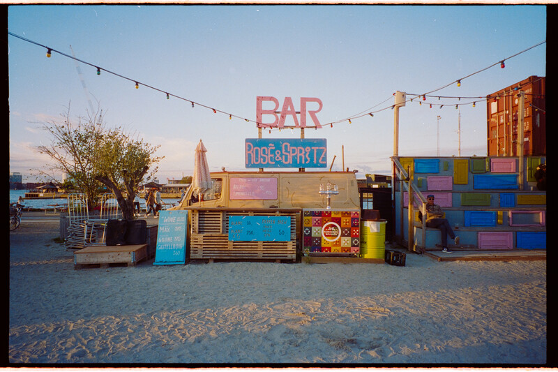 Colorful shipping container bar and restaurant structure on a beach at golden hour.