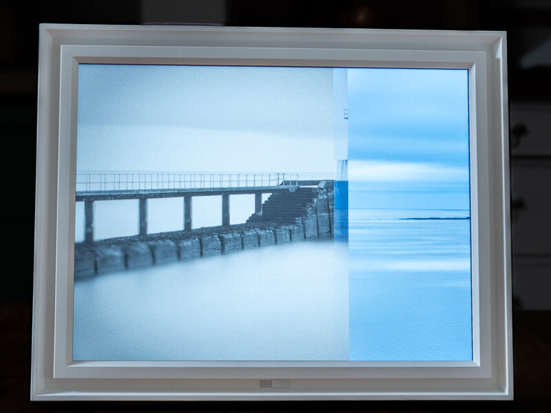 Long exposure photograph of a concrete pier extending into calm blue ocean water under clear sky.