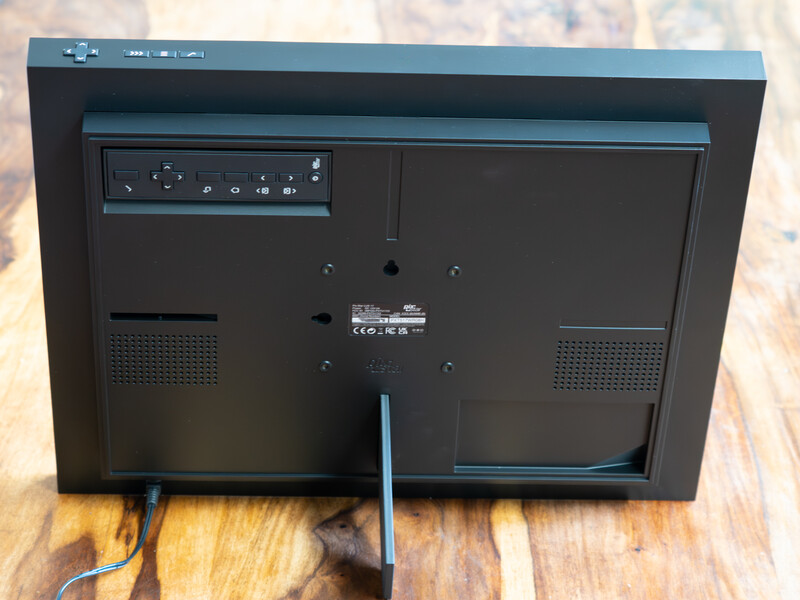 Rear view of a flat-panel monitor showing ports, cable management, and ventilation grilles on wooden surface.