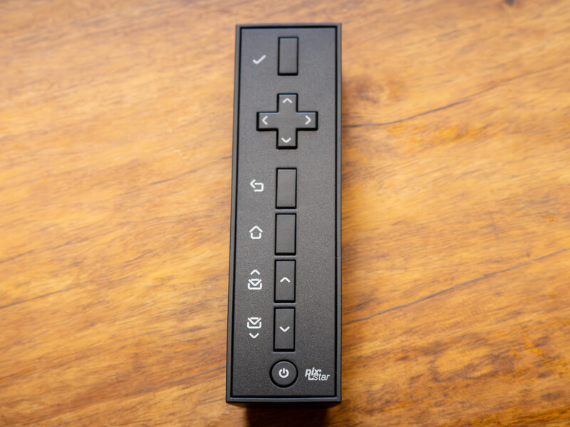 Nintendo Wii remote control with black finish, showing directional pad, action buttons, and motion controls on wooden surface.