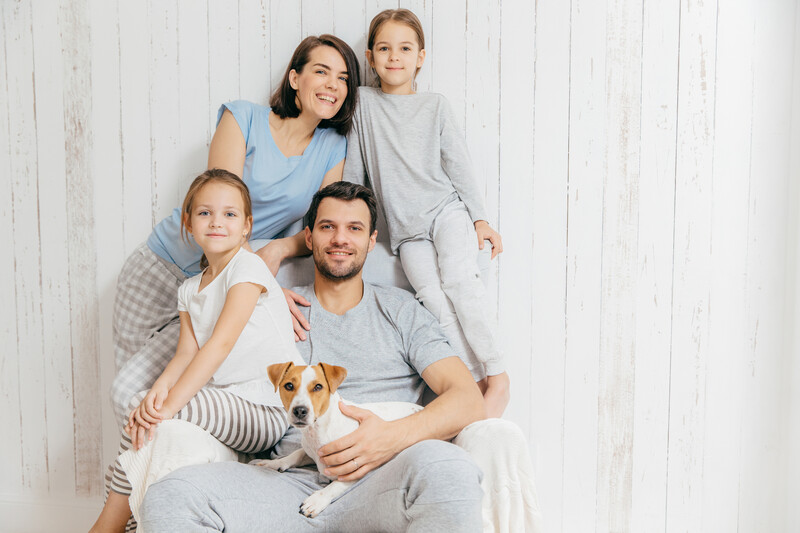 Family of four with a dog posed together against a white shiplap wall.