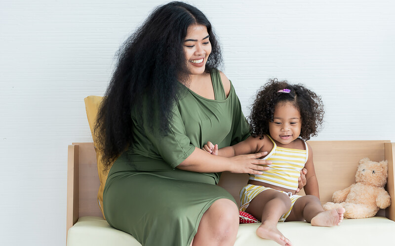 Woman and young child sitting together on a neutral beige couch against a white background.