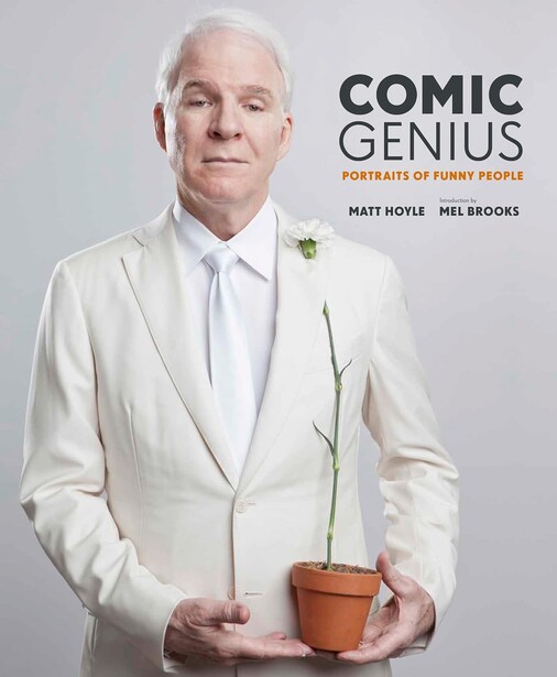Man in white suit holding potted plant against neutral background.