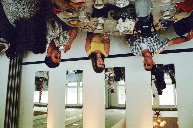 Four people seated at a dining table during a meal in a bright, minimalist interior space.