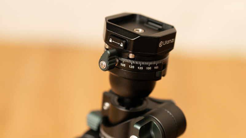 Ball head tripod mount with panoramic rotation scale and adjustment knobs against beige background.