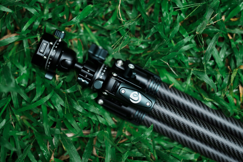 Carbon fiber tripod head with fluid ball mount and pan-tilt controls on grass.