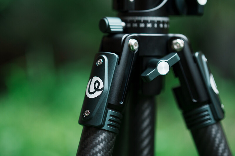 Close-up of a professional tripod head with ball mount and pan-tilt controls against a blurred green background.