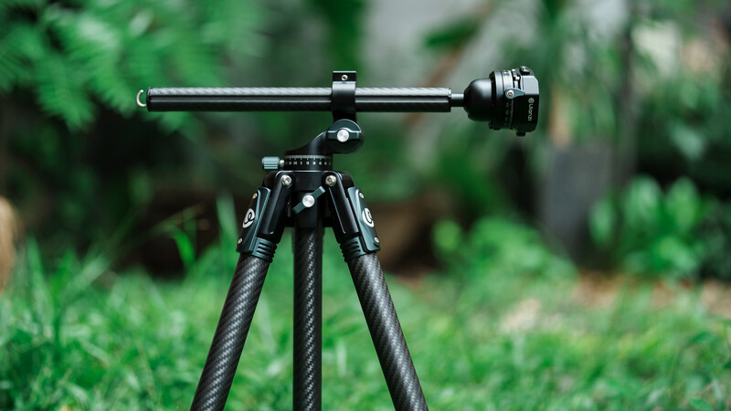 Carbon fiber tripod with horizontal jib arm and ball head mounted outdoors on grass.