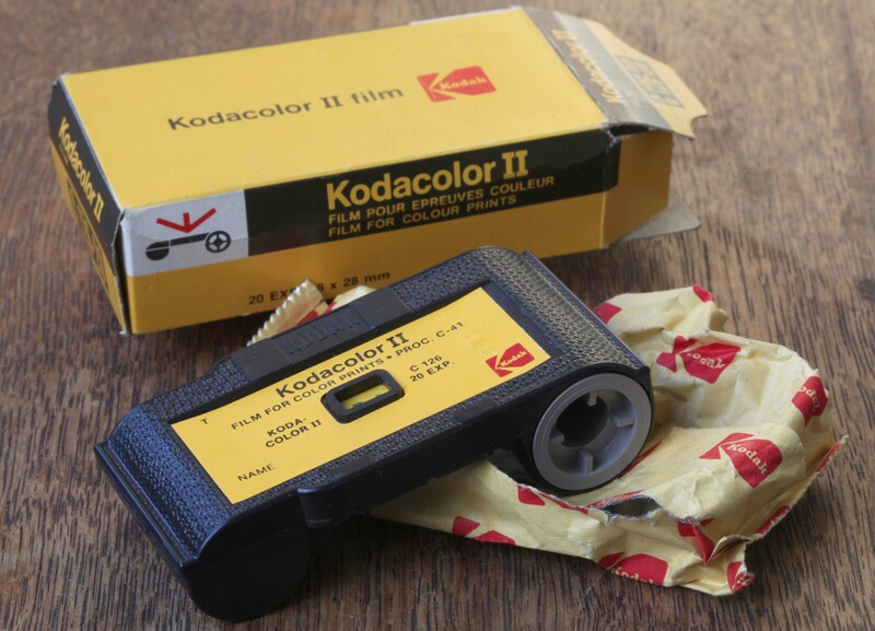 Kodacolor II film camera with original yellow box packaging and protective cloth wrapping on wooden surface.