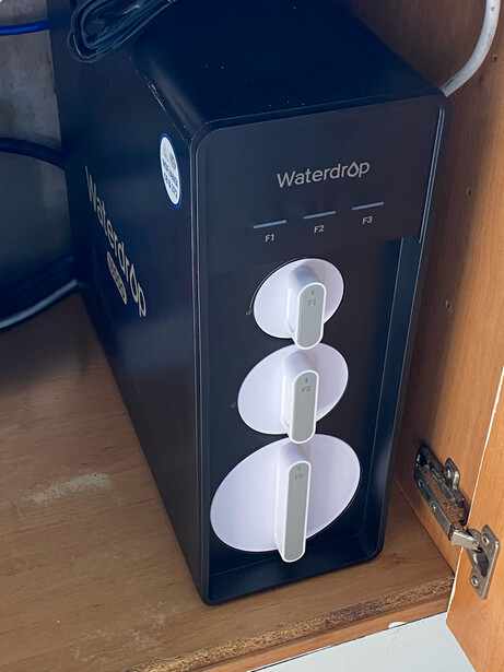 Black desktop water dispensing system with three white cup holders stacked vertically.